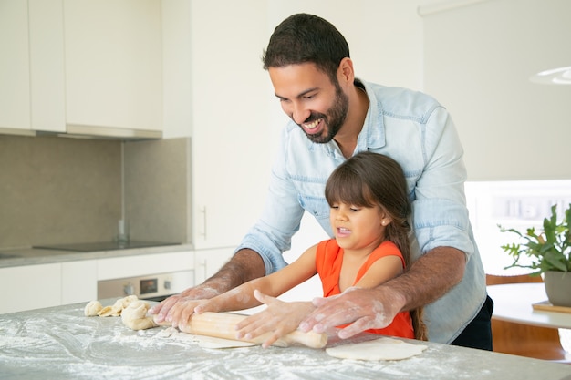 Foto gratuita feliz papá e hija rodando masa en la mesa de la cocina con harina desordenada.