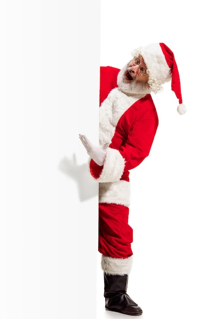 Feliz Papá Noel sorprendido apuntando sobre fondo de banner de publicidad en blanco con espacio de copia. Hombre mayor sonriente que muestra en blanco en blanco del cartel vacío