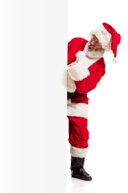 Feliz Papá Noel sorprendido apuntando sobre fondo de banner de publicidad en blanco con espacio de copia. Hombre mayor sonriente que muestra en blanco en blanco del cartel vacío