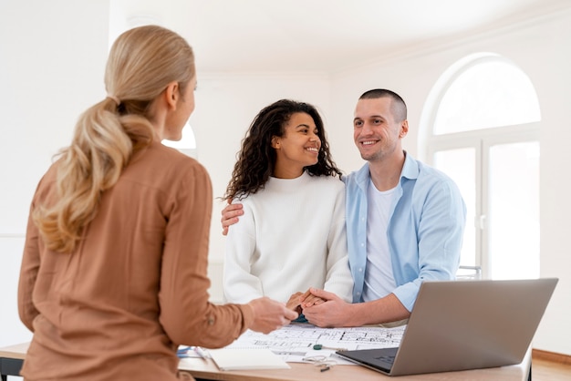 Feliz pareja abrazada conversando con inmobiliaria femenina