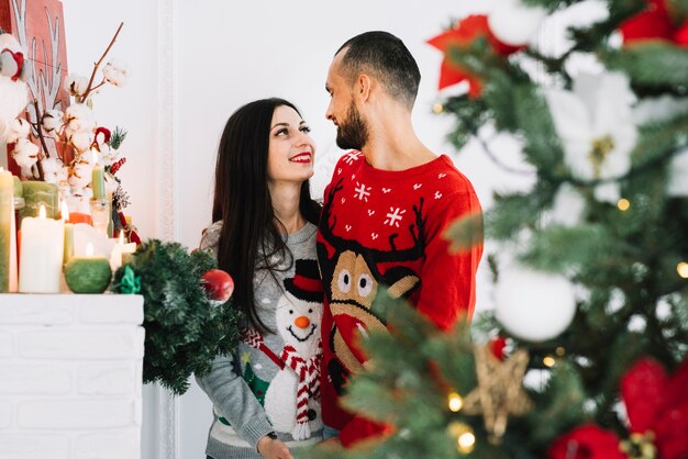 Feliz pareja abrazándose cerca de velas y abeto