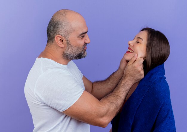 Feliz pareja adulta mujer envuelta en un chal sonriendo con los ojos cerrados hombre mirándola y pellizcando sus mejillas