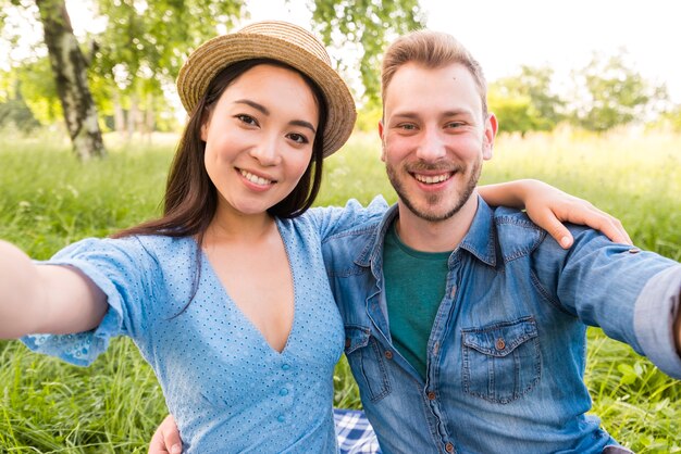 Feliz pareja adulta multirracial tomando selfie en el parque