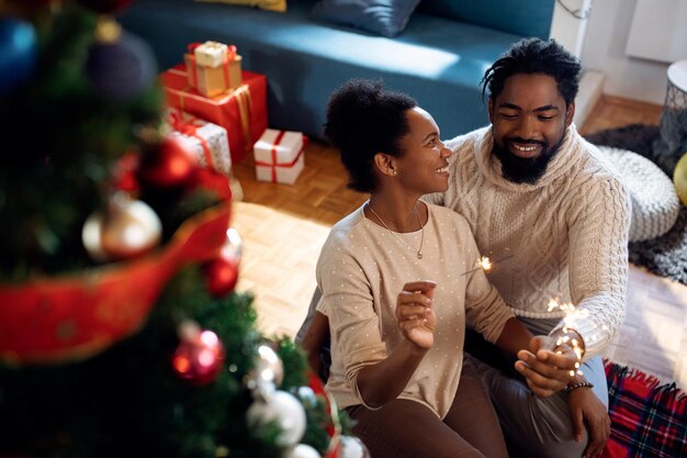 Feliz pareja afroamericana divirtiéndose con bengalas el día de Navidad en casa