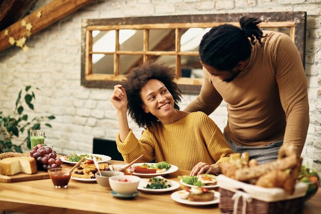 Feliz pareja afroamericana hablando mientras come en la mesa del comedor