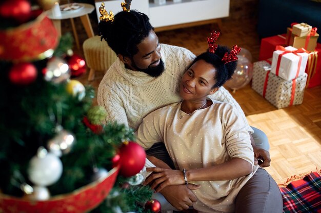 Feliz pareja afroamericana relajándose junto al árbol de Navidad en casa