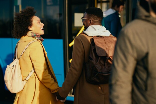 Feliz pareja afroamericana tomándose de la mano y hablando en la estación de autobuses