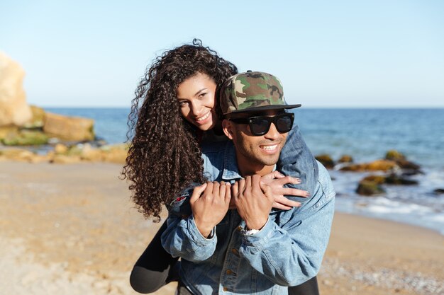 Feliz pareja amorosa africana caminando al aire libre en la playa