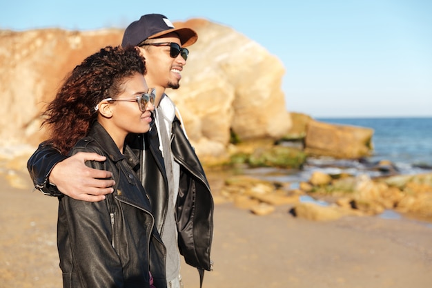 Feliz pareja amorosa africana caminando al aire libre en la playa