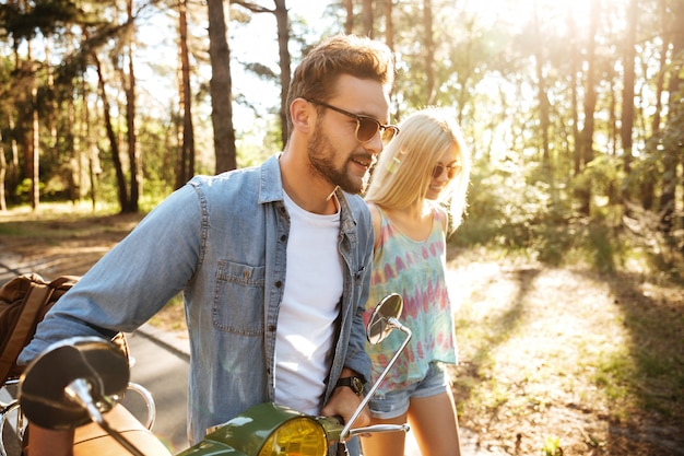 Feliz pareja amorosa caminando con scooter al aire libre