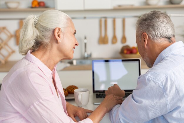 Feliz pareja amorosa madura familia en la cocina usando laptop