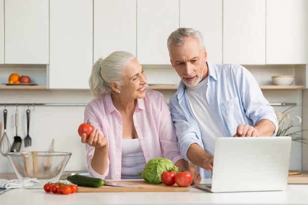 Feliz pareja amorosa madura familia usando laptop y cocina