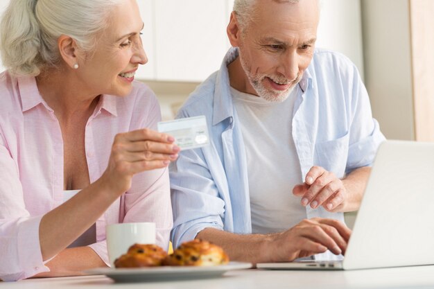 Feliz pareja amorosa madura familia usando laptop con tarjeta de crédito