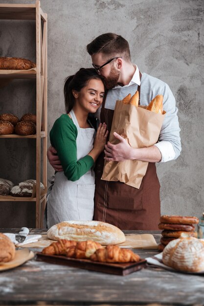 Feliz pareja amorosa panaderos de pie cerca de pan y abrazos