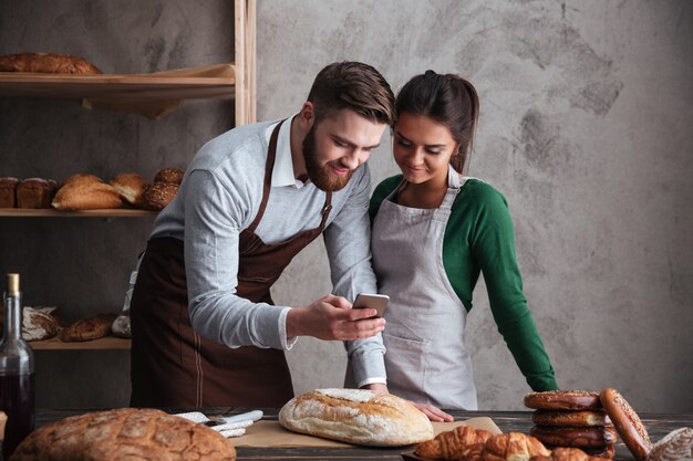 Feliz pareja amorosa panaderos de pie cerca de pan con teléfono