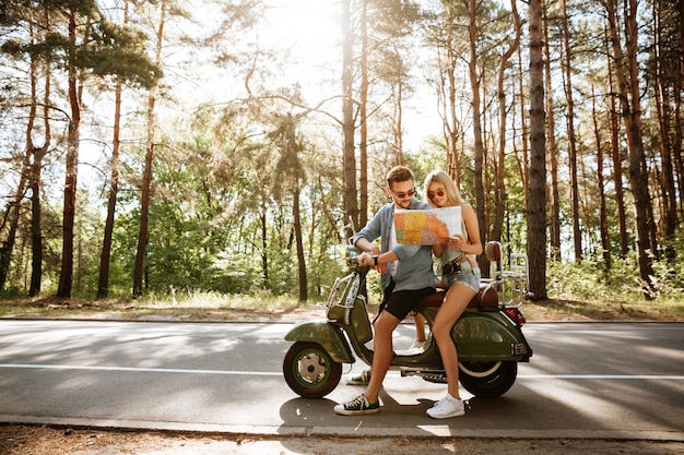 Feliz pareja amorosa sosteniendo mapa al aire libre cerca de scooter