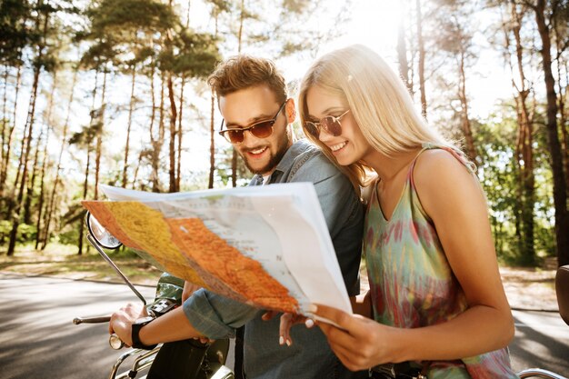 Feliz pareja amorosa sosteniendo mapa al aire libre cerca de scooter
