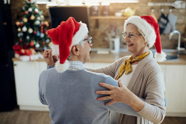 Feliz pareja de ancianos bailando mientras celebra la Navidad en casa