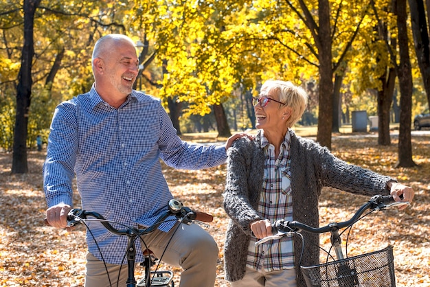 Feliz pareja de ancianos en bicicleta en el parque en otoño