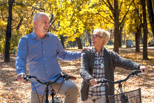 Feliz pareja de ancianos en bicicleta en el parque en otoño