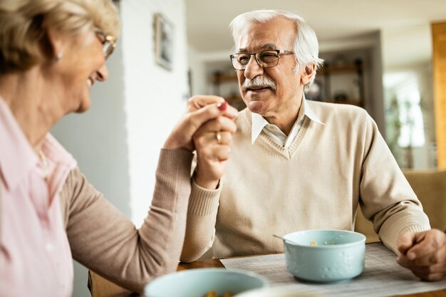 Feliz pareja de ancianos comunicándose mientras se toman de la mano en la mesa del comedor