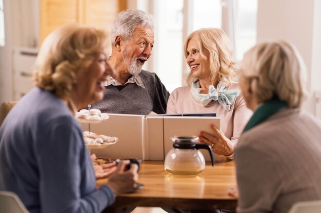 Feliz pareja de ancianos hablando y divirtiéndose mientras miran su álbum de fotos en casa