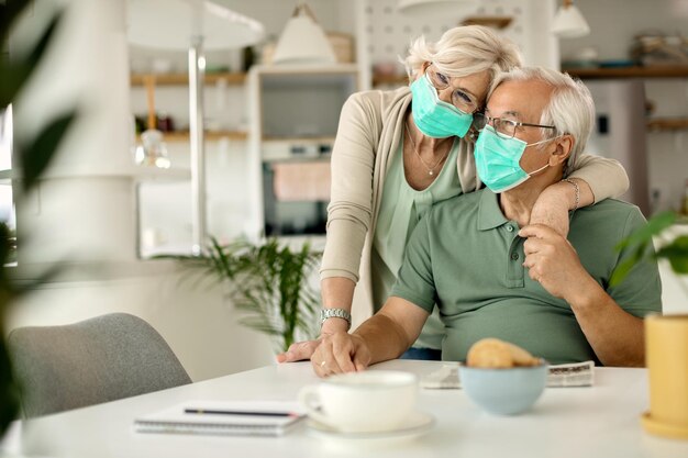 Feliz pareja de ancianos con mascarillas protectoras abrazándose en casa