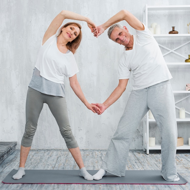 Feliz pareja de ancianos de pie en la estera de yoga en casa