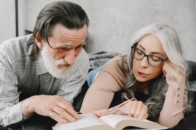 Feliz pareja de ancianos relajándose juntos en casa. Libro de lectura de los pares mayores en la cama.