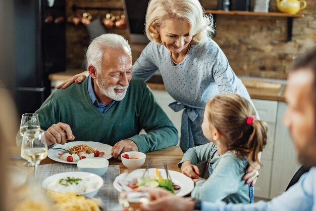 Feliz pareja de ancianos y su nieta comunicándose durante una comida en el comedor