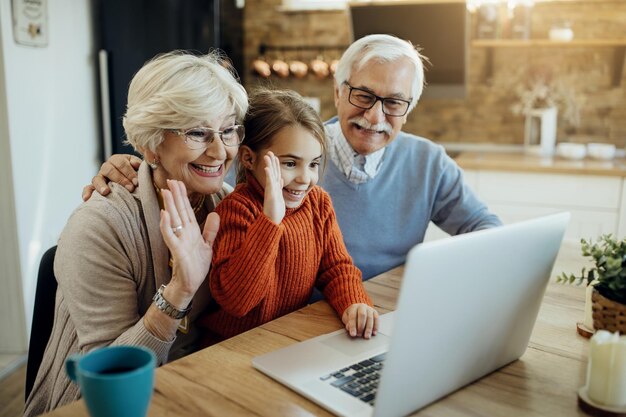 Feliz pareja de ancianos y su nieta usando laptop y haciendo videollamadas en casa