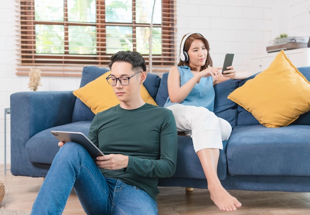 Feliz pareja asiática pasa el fin de semana juntos en el sofá en el interior de su casa, relajándose y disfrutando de la navegación por Internet.