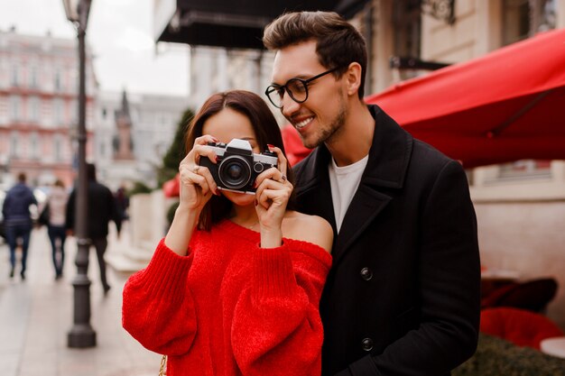 Feliz pareja avergonzada y posando en la calle de vacaciones. Estado de ánimo romántico. Hermosa mujer morena con cámara de película.