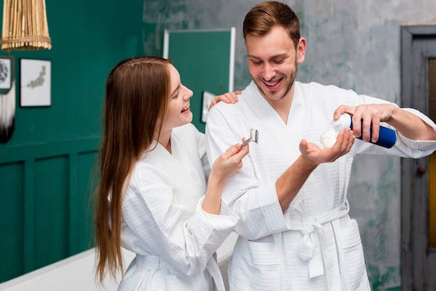 Feliz pareja en batas de baño con espuma de afeitar