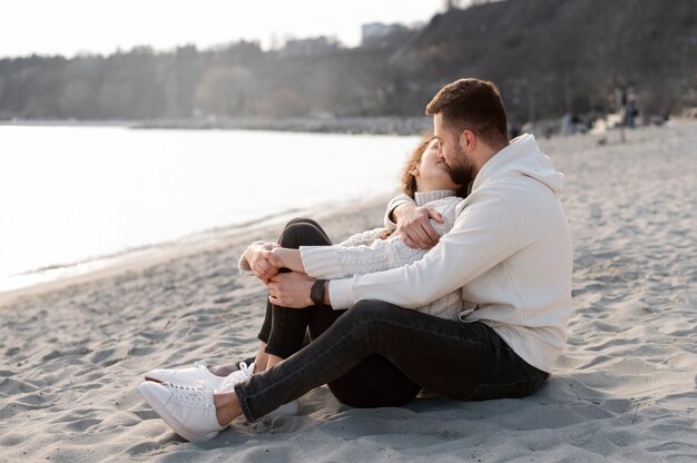 Feliz pareja besándose en la playa tiro completo