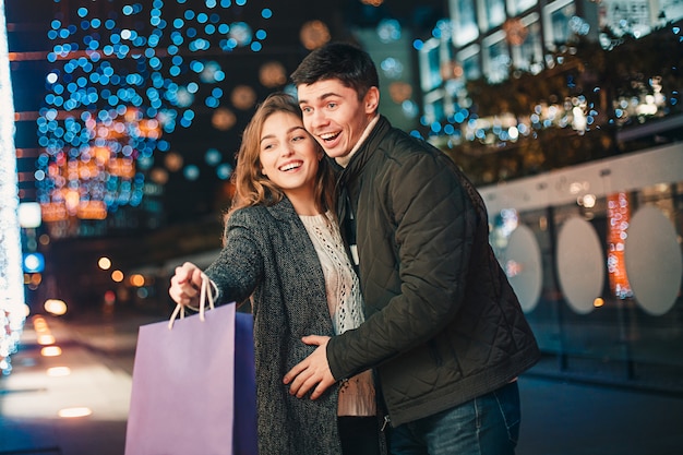 La feliz pareja con bolsas de compras disfrutando de la noche en la ciudad