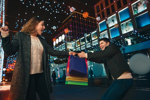 La feliz pareja con bolsas de compras disfrutando de la noche en la ciudad