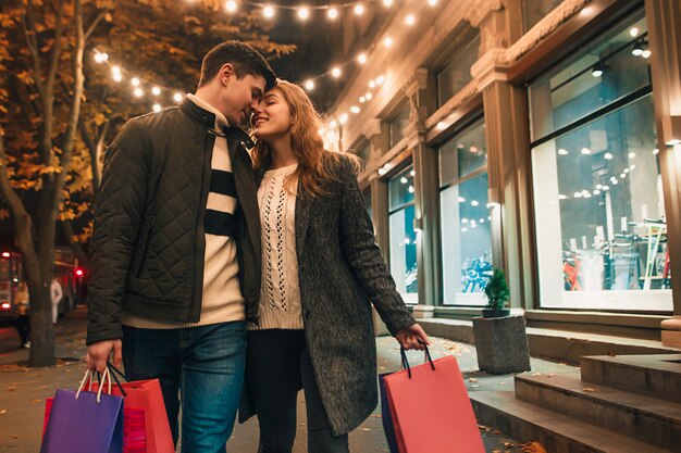 La feliz pareja con bolsas de compras disfrutando de la noche en la ciudad