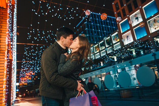 La feliz pareja con bolsas de compras disfrutando de la noche en el fondo de la ciudad