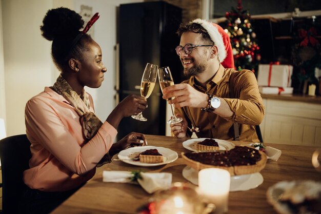 Feliz pareja brindando con champán durante la cena de Navidad en el comedor