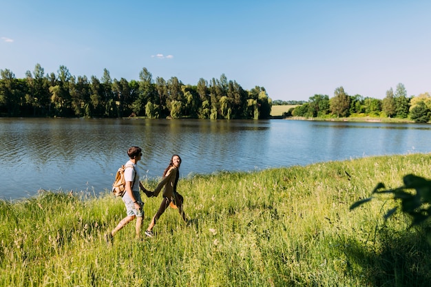 Feliz pareja caminando en la hierba verde cerca del lago idílico