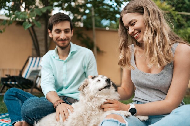 Feliz pareja de chicos jugando con su perro en el patio trasero sobre la hierba. Perro viejo alegre