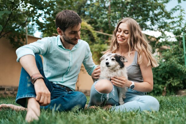 Feliz pareja de chicos jugando con su perro en el patio trasero sobre la hierba. Perro viejo alegre