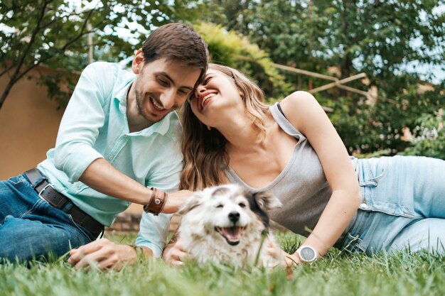 Feliz pareja de chicos jugando con su perro en el patio trasero sobre la hierba. Perro viejo alegre