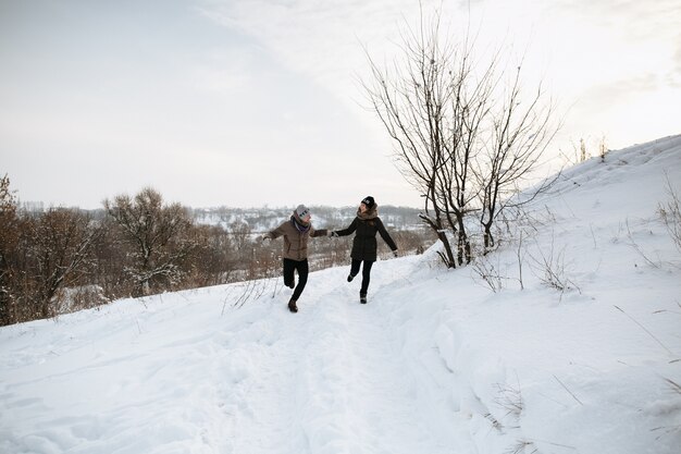 Feliz pareja corre tomados de la mano en un día de invierno cubierto de nieve. Amor de invierno Historia de amor.