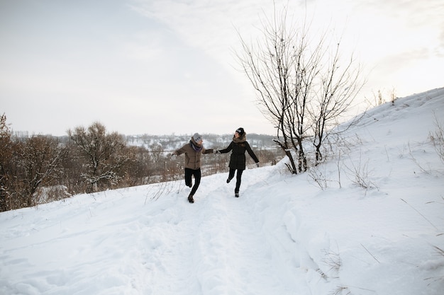 Feliz pareja corre tomados de la mano en un día de invierno cubierto de nieve. Amor de invierno Historia de amor.