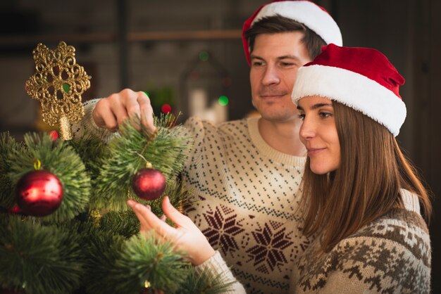 Feliz pareja decorando el árbol de navidad con globos