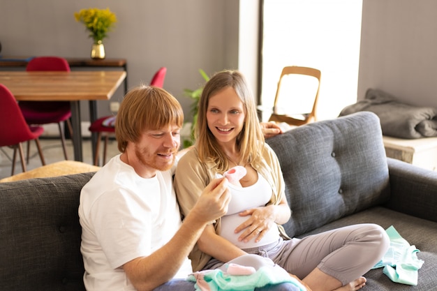 Feliz pareja embarazada comprobando la ropa del bebé en la sala de estar