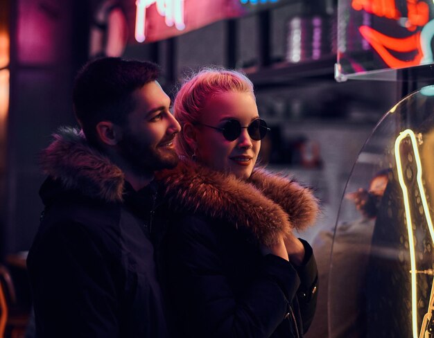 Feliz pareja enamorada. Una chica hermosa y un hombre guapo parados en la noche en la calle. Letreros iluminados, neón, luces.