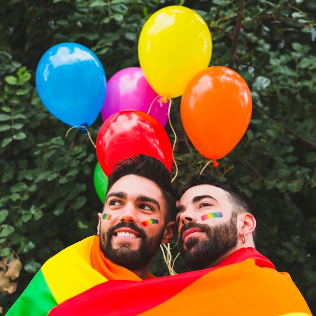 Feliz pareja gay con globos LGBT abrazándose en el jardín